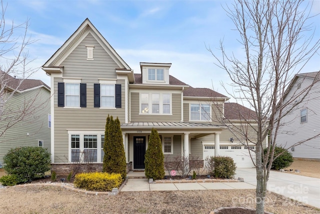 view of front facade with a porch, concrete driveway, metal roof, a garage, and stone siding