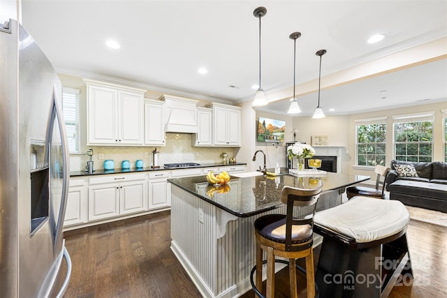 kitchen with a sink, stainless steel fridge with ice dispenser, gas cooktop, custom range hood, and ornamental molding