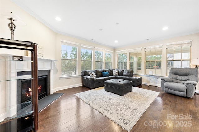 living room featuring dark wood finished floors, crown molding, a glass covered fireplace, and a healthy amount of sunlight