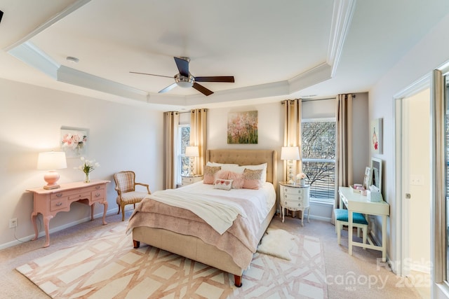 bedroom with a raised ceiling, light colored carpet, ceiling fan, and multiple windows