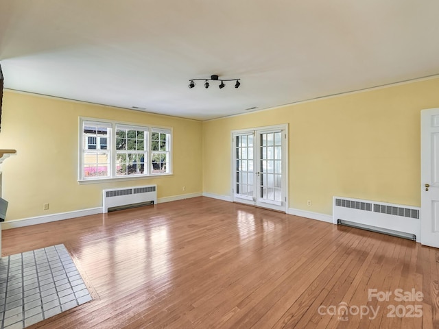 unfurnished living room with radiator, rail lighting, wood-type flooring, and french doors