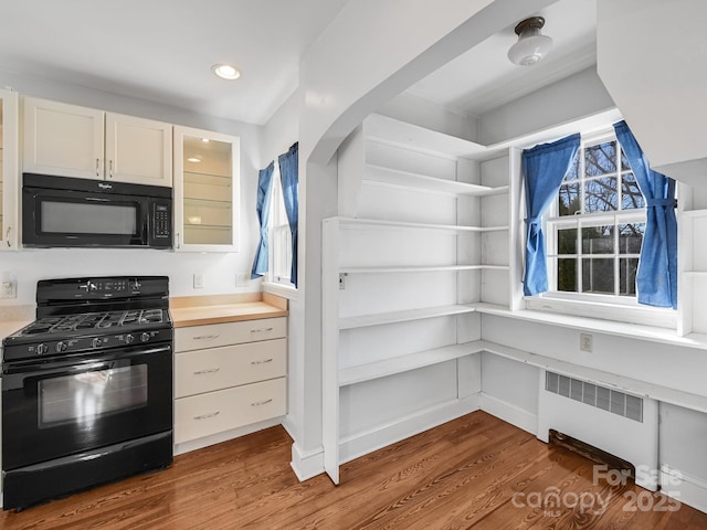 kitchen featuring a wealth of natural light, radiator, hardwood / wood-style floors, and black appliances