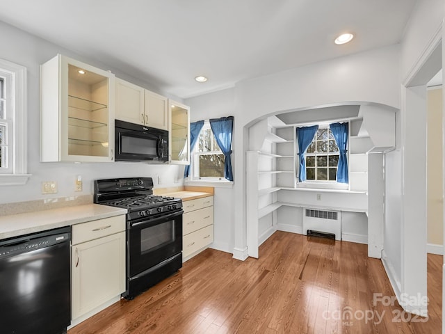 kitchen with radiator, black appliances, and light wood-type flooring