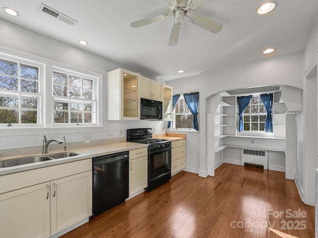 kitchen featuring radiator, sink, dark hardwood / wood-style flooring, ceiling fan, and black appliances