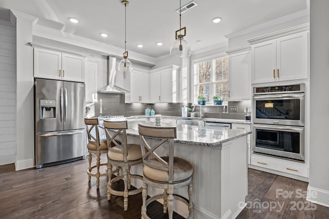 kitchen with appliances with stainless steel finishes, white cabinetry, a kitchen island, and wall chimney range hood