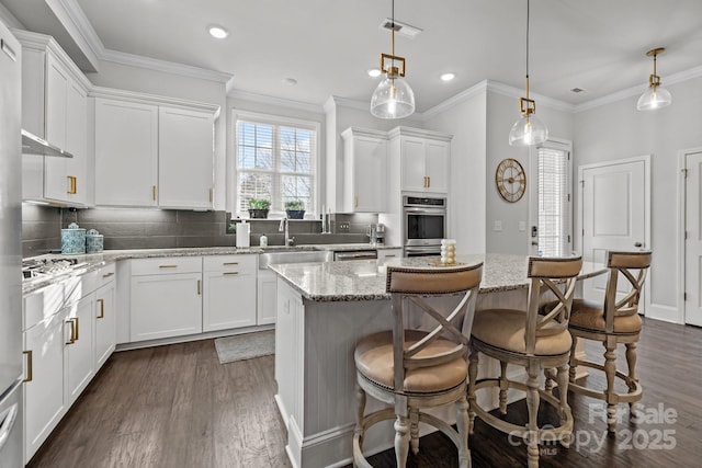 kitchen featuring light stone counters, decorative light fixtures, white cabinetry, and a center island