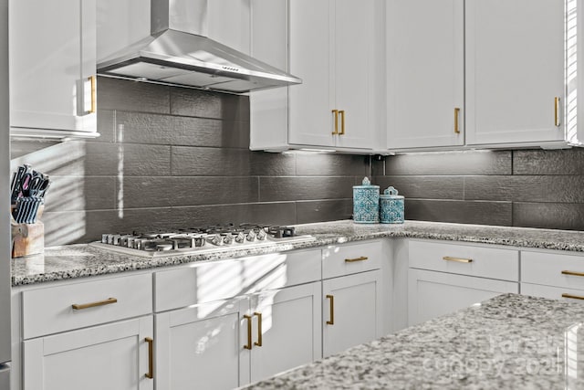 kitchen featuring white cabinetry, light stone countertops, wall chimney range hood, and stainless steel gas stovetop