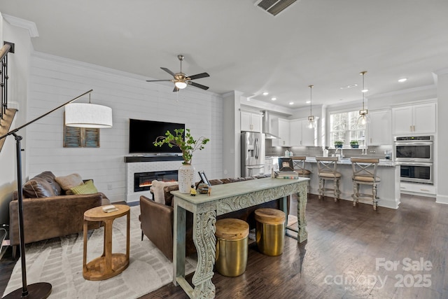 living room featuring ceiling fan, dark wood-type flooring, wood walls, and crown molding