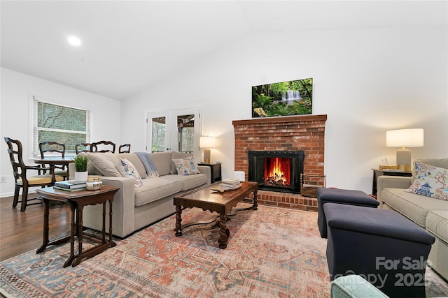 living room with vaulted ceiling, a brick fireplace, and hardwood / wood-style floors