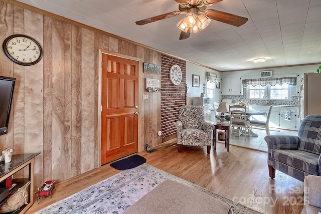 living room featuring crown molding, wooden walls, ceiling fan, and light wood-type flooring