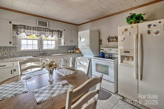 kitchen with white cabinetry, white appliances, stacked washer / dryer, and light tile patterned floors