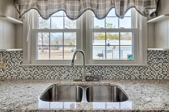 interior details with tasteful backsplash, sink, and light stone countertops