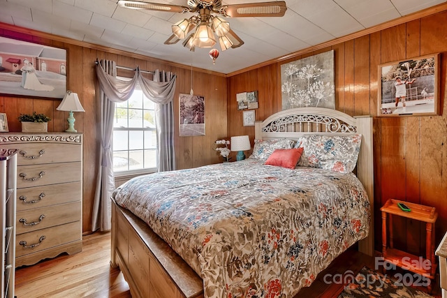 bedroom featuring ornamental molding, wooden walls, ceiling fan, and light wood-type flooring