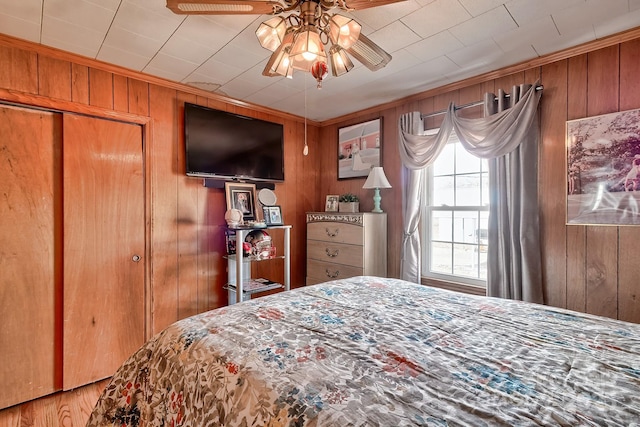 bedroom with ceiling fan, ornamental molding, and wooden walls