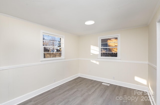 empty room featuring ornamental molding, visible vents, baseboards, and wood finished floors