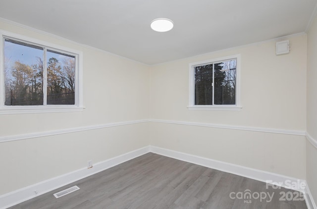 spare room with baseboards, wood finished floors, visible vents, and crown molding