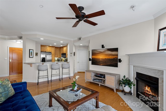 living room with crown molding, a high end fireplace, ceiling fan, and light wood-type flooring