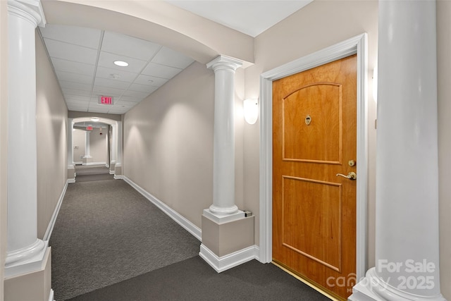 hall with a paneled ceiling, decorative columns, and dark colored carpet