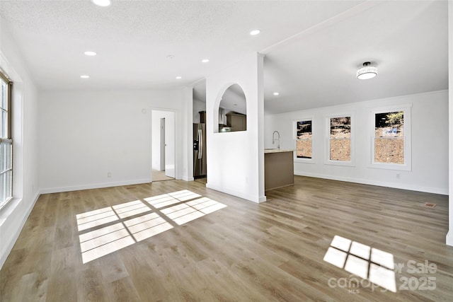 unfurnished living room featuring sink, a textured ceiling, lofted ceiling, and light wood-type flooring