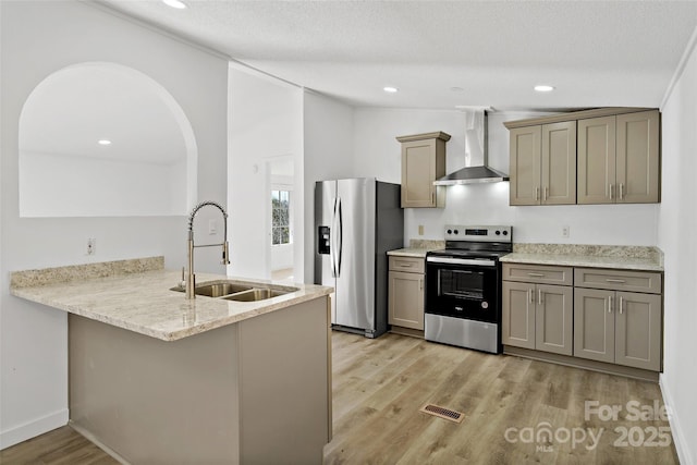 kitchen with a textured ceiling, wall chimney range hood, stainless steel appliances, sink, and kitchen peninsula