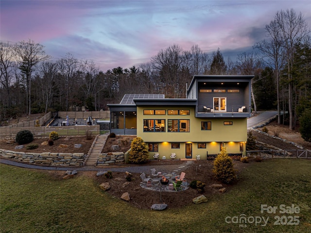 back house at dusk with solar panels, a sunroom, a yard, and an outdoor fire pit