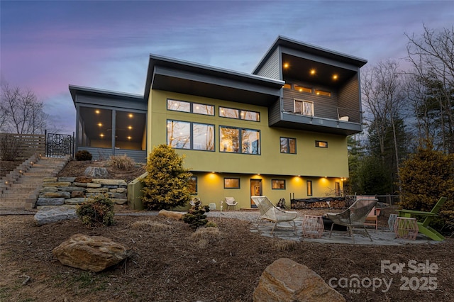 back house at dusk featuring a balcony, a sunroom, a fire pit, and a patio area