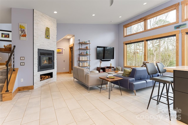 tiled living room featuring a stone fireplace and a towering ceiling