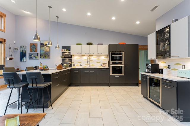 kitchen with decorative light fixtures, white cabinetry, sink, beverage cooler, and a kitchen bar