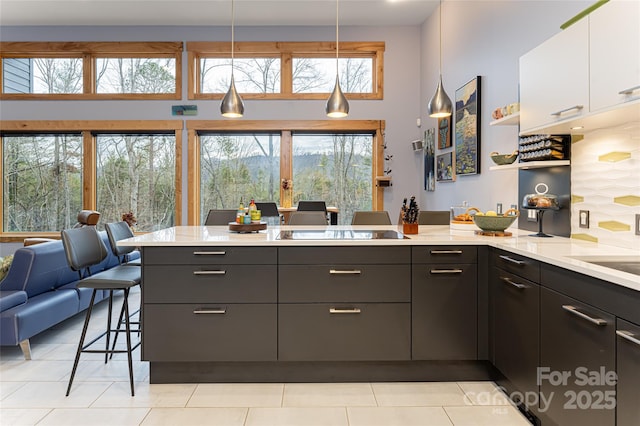 kitchen featuring a kitchen bar, hanging light fixtures, white cabinets, a healthy amount of sunlight, and a high ceiling