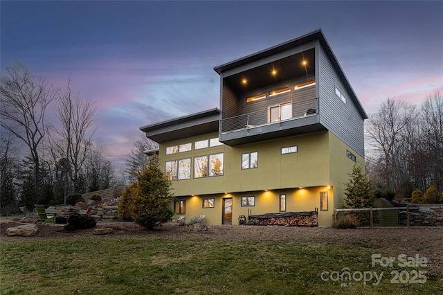 back house at dusk featuring a balcony and a yard