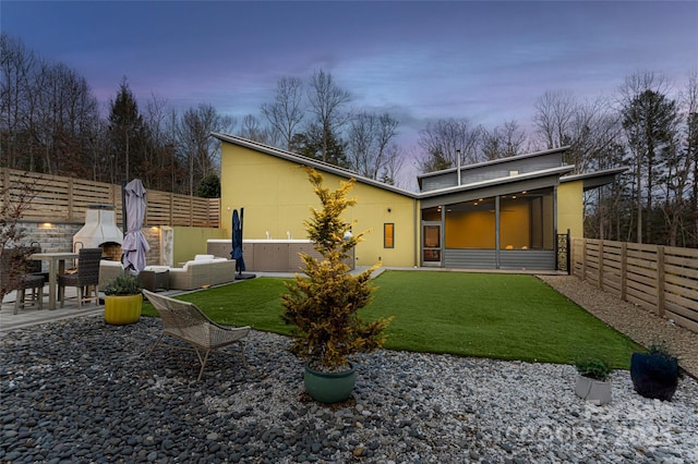 back house at dusk featuring a jacuzzi, a sunroom, a patio, and an outdoor living space with a fireplace