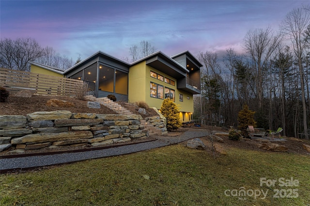 property exterior at dusk with a sunroom and a lawn