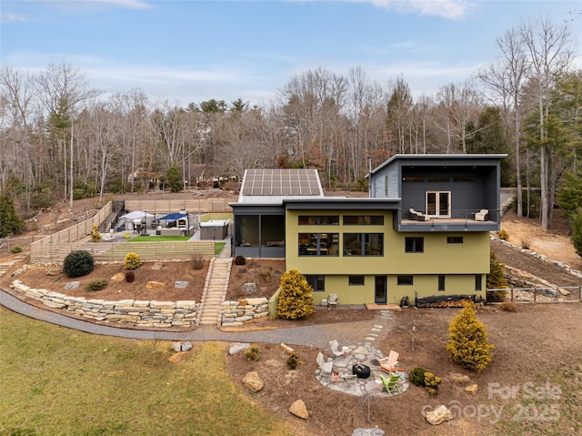 rear view of property with solar panels, a balcony, a sunroom, and an outdoor fire pit