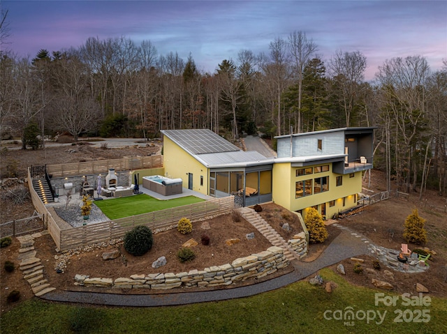 back house at dusk with a patio area, a hot tub, and solar panels