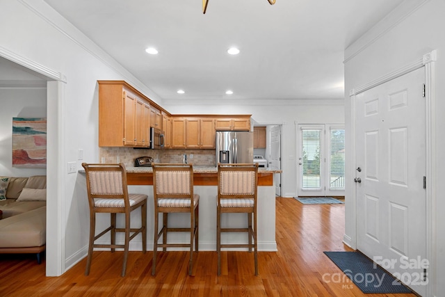 kitchen with kitchen peninsula, crown molding, stainless steel appliances, and light wood-type flooring