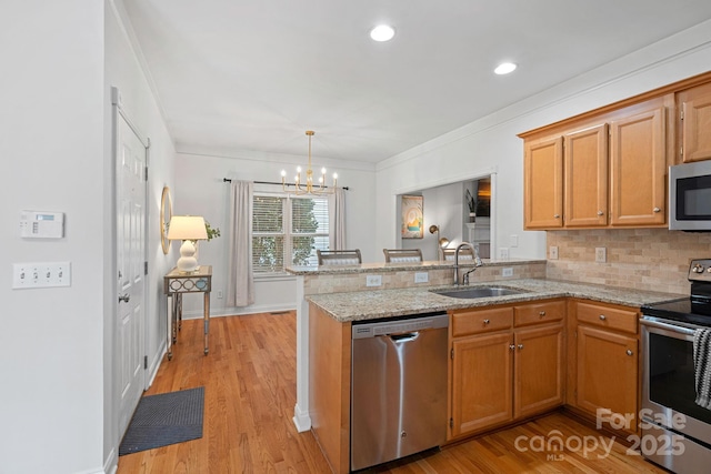 kitchen featuring kitchen peninsula, sink, light wood-type flooring, stainless steel appliances, and light stone counters