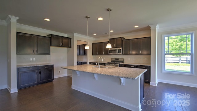 kitchen featuring sink, hanging light fixtures, a kitchen island with sink, stainless steel appliances, and ornamental molding