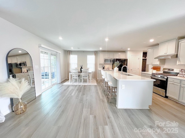 kitchen featuring a kitchen bar, sink, white cabinetry, appliances with stainless steel finishes, and a kitchen island with sink