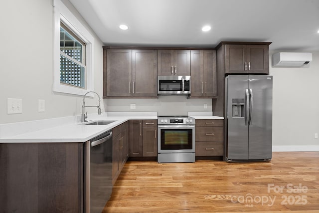 kitchen featuring sink, light wood-type flooring, an AC wall unit, and appliances with stainless steel finishes