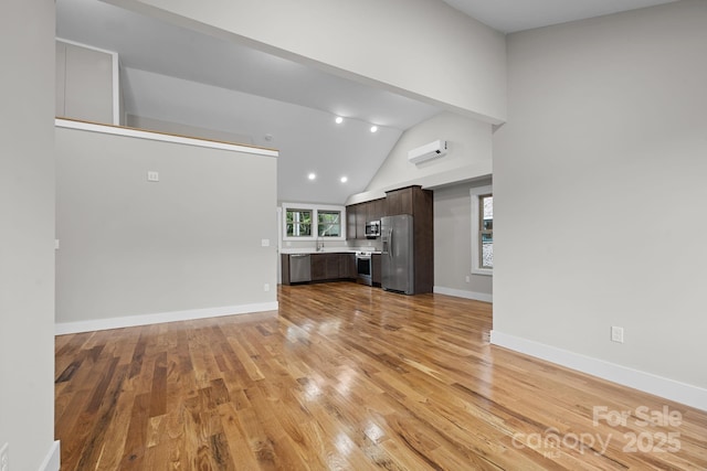 unfurnished living room with high vaulted ceiling, sink, an AC wall unit, and light wood-type flooring