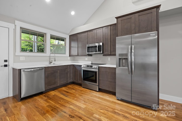 kitchen with light hardwood / wood-style floors, appliances with stainless steel finishes, sink, dark brown cabinets, and vaulted ceiling