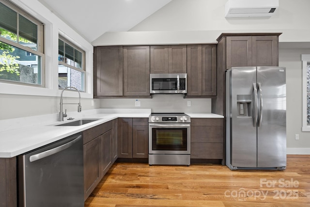 kitchen featuring lofted ceiling, stainless steel appliances, light hardwood / wood-style floors, sink, and a wall unit AC