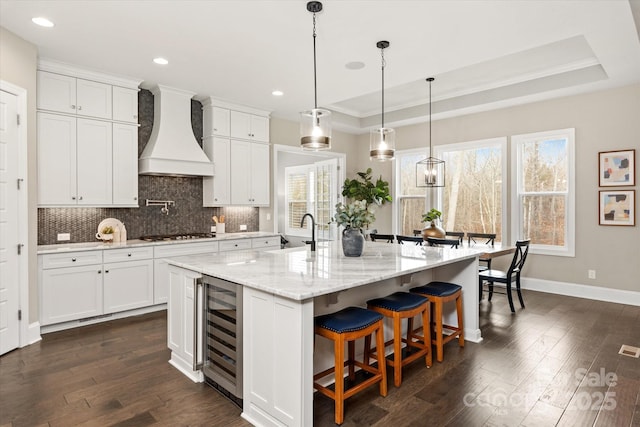 kitchen featuring premium range hood, a tray ceiling, a large island, and white cabinets