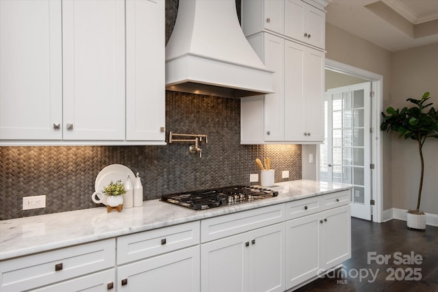 kitchen with white cabinetry, light stone countertops, custom range hood, stainless steel gas cooktop, and decorative backsplash