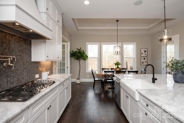 kitchen with sink, appliances with stainless steel finishes, premium range hood, white cabinets, and a raised ceiling