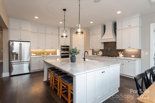 kitchen featuring white cabinetry, appliances with stainless steel finishes, custom exhaust hood, and a center island with sink