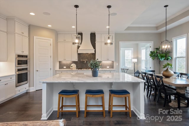 kitchen with a large island, a tray ceiling, and custom range hood