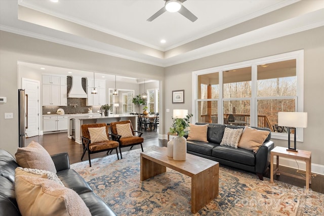 living room with ceiling fan, ornamental molding, a tray ceiling, and dark hardwood / wood-style flooring