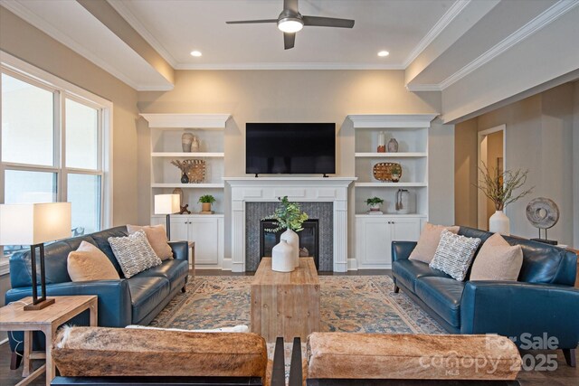 living room with a tile fireplace, ornamental molding, ceiling fan, light hardwood / wood-style floors, and built in shelves