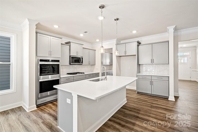 kitchen featuring decorative light fixtures, gray cabinets, sink, an island with sink, and stainless steel appliances